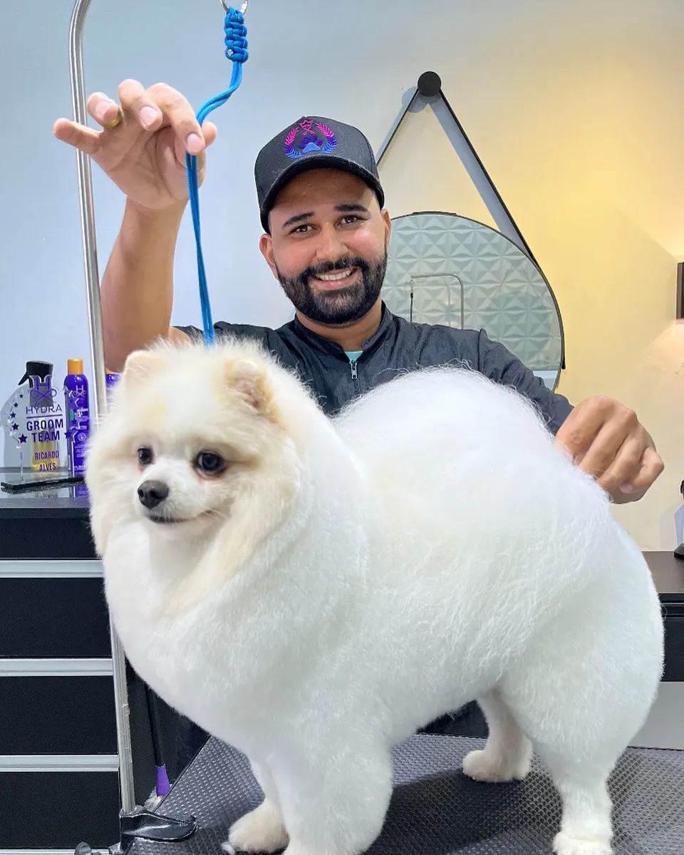 Profissional sorrindo ao lado de um cão de pelagem branca e volumosa após a escovação